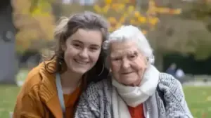 accueil Deux personnes de générations différentes souriant côte à côte dans un parc d’automne, exprimant complicité et douceur.